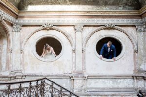 Fotografia ślubna Małopolska – para młoda wyglądająca z okrągłych okien zabytkowego pałacu