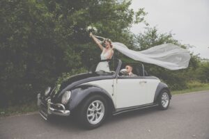 Fotografia ślubna Nowy Targ – radosna panna młoda wystawiona z kabrioletu z uniesionym welonem