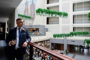 przygotowania ślubne Kraków - elegancki pan młody z drinkiem na balkonie hotelu z widokiem na miasto